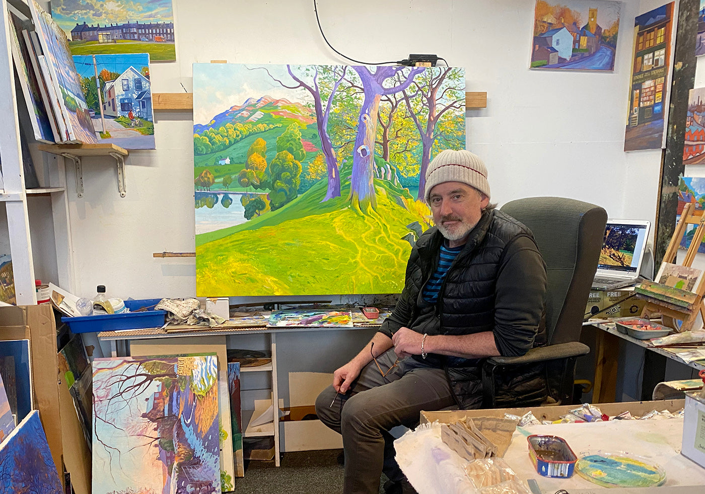 Chris Cyprus Artist sitting in his art studio with paintings on the walls and desk.