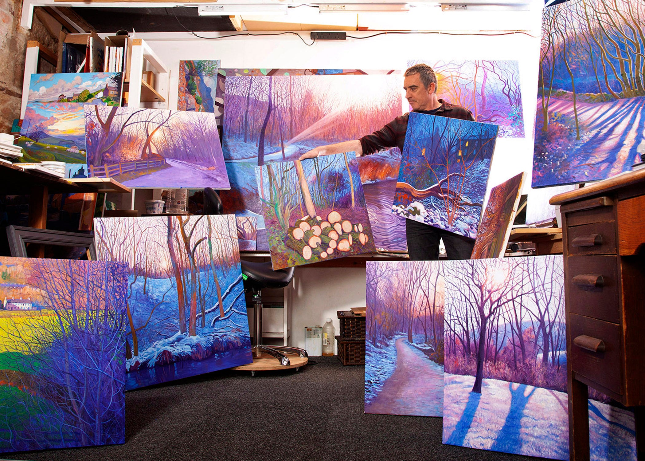 Artist Chris Cyprus in his studio surrounded by paintings 